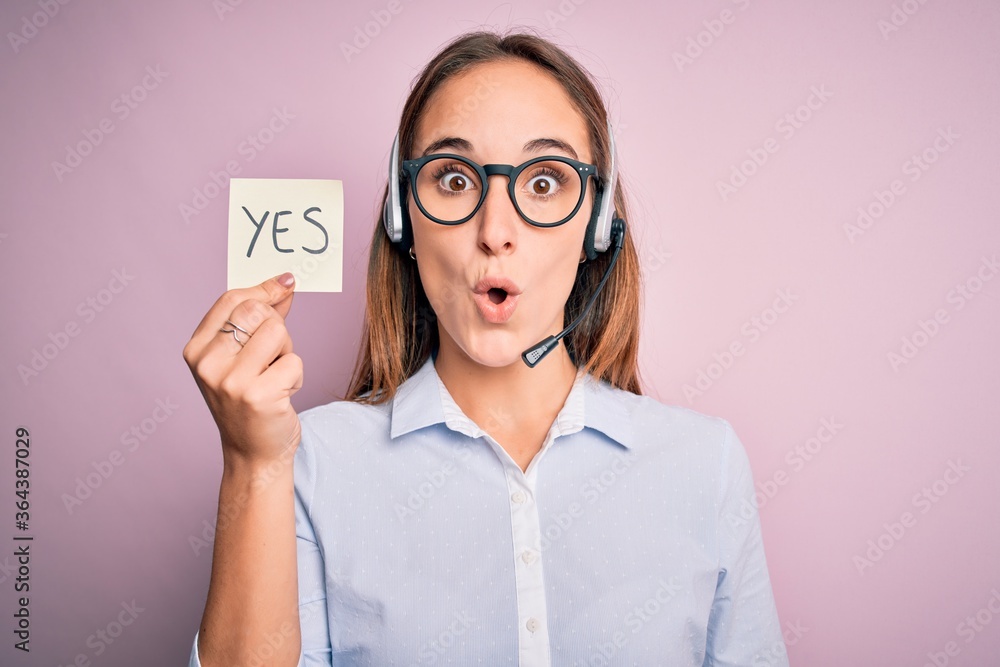 Beautiful call center agent woman working using headset holding reminder with yes message scared in shock with a surprise face, afraid and excited with fear expression Beautiful call center agent woman working using headset holding reminder with yes message scared in shock with a surprise face, afraid and excited with fear expression