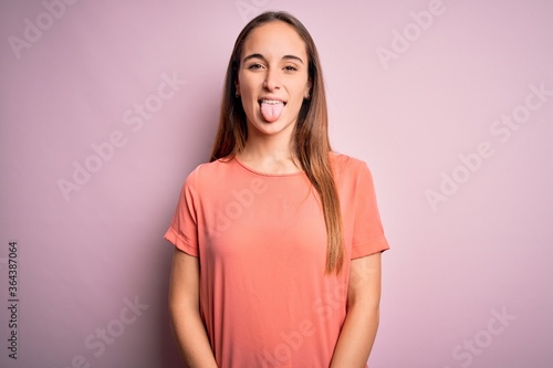 Young beautiful woman wearing casual t-shirt standing over isolated pink background sticking tongue out happy with funny expression. Emotion concept.
