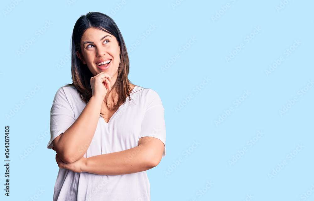 Young beautiful brunette woman wearing casual t-shirt looking confident at the camera with smile with crossed arms and hand raised on chin. thinking positive.