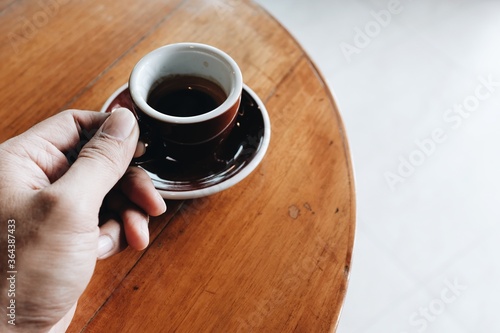 Close-up view of a man's left hand holding an espresso in a coffee shop