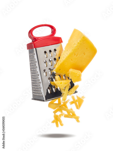 Piece of cheese is rubbed on metal hand grater. Slices of cheese and grater levitate in air. Grater and cheese isolated on white background.
