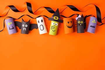 Halloween and decoration concept - monsters from toilet paper roll tube on orange. Simple easy diy creative idea. Eco-friendly reuse recycle decor, kindergarten paper craft, seasonal holiday banner