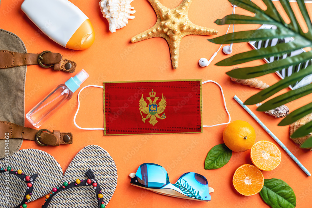 Obraz premium Accessories for beach holidays around a protective mask with the flag of Montenegro. Concept of leisure at sea during a pandemic. Top view