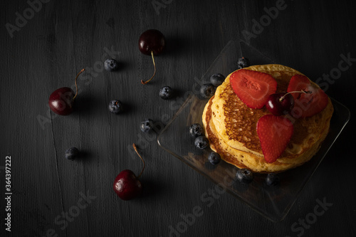 Hot Cakes apilados con cerezas fresas y arandanos sobre una mesa de madera color negro vintage. Espacio para texto  photo