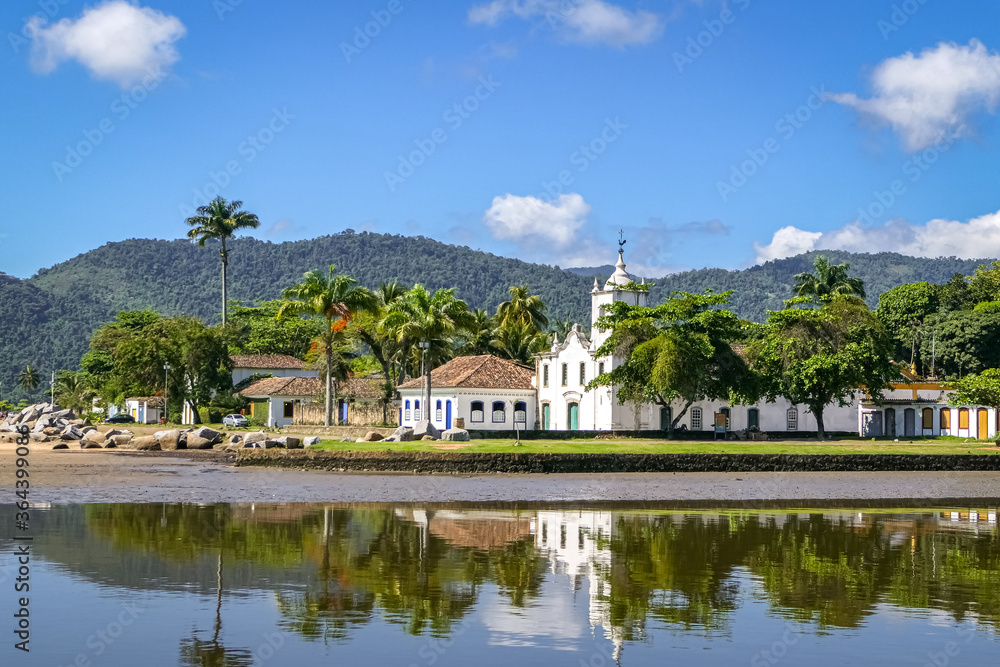 Panoramic view of colonial church Igreja Nossa Senhora das Dores (Church of Our Lady of Sorrows) with water reflections and mountains in background, historic town Paraty, Brazil