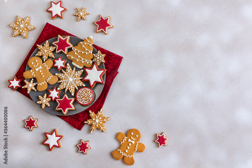 Top view of gingerbread cookies on plate and white snowy background with copy space. Tasty glazed painted cookies: snowflakes, stars, gingerbread man. Merry Christmas and Happy New Year!