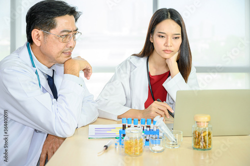 Couple of Asian adult male doctor and Asian young female doctor wearing formal white coat teamwork brainstorm meeting with computer laptop at the hospital.