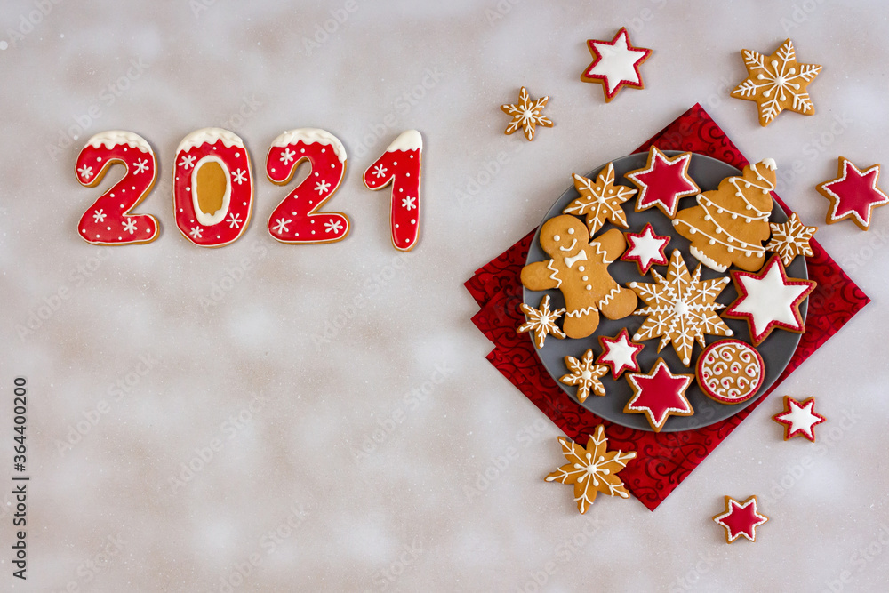 Top view of christmas gingerbread cookies on grey plate on white snowing background. Glazed painted cookies: snowflakes, stars, gingerbread man, numbers. Merry Christmas and Happy New Year 2021.