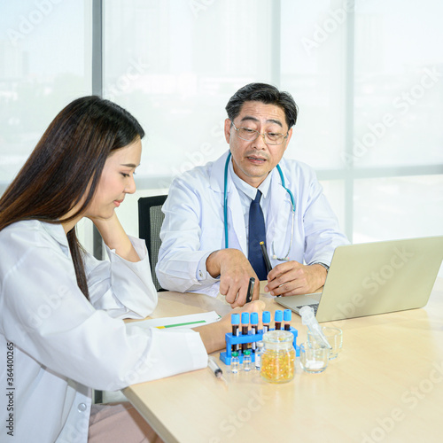 Couple of Asian adult male doctor and Asian young female doctor wearing formal white coat teamwork brainstorm meeting with computer laptop at the hospital.