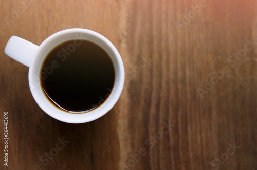 Top view of a black coffee ( americano ) in coffee cup on wood background, soft focus with sun ray light