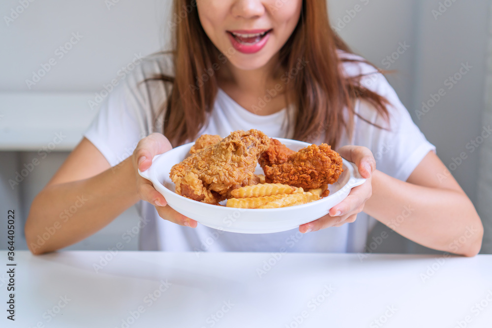 Young Asian woman in white T-shirt holding a plate of her favorite fried chicken, french fries. Unhealthy food concept. Close up