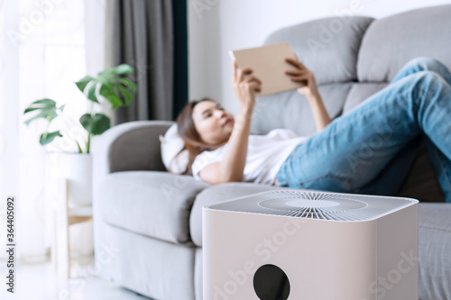 Close up of white air purifier on the floor in living room the background of young Asian woman relaxes. Concept of caring for fresh air at home. Caring for well-being and health. Air filter. photo