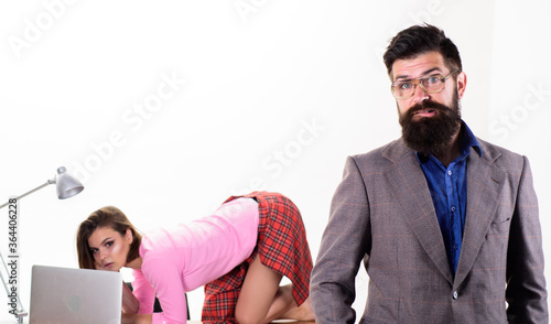 Doubting manager. Project manager and sexy coworker on office desk. General manager with pretty employee working on laptop in background. Brutal caucasian man with long beard in formal manager outfit photo