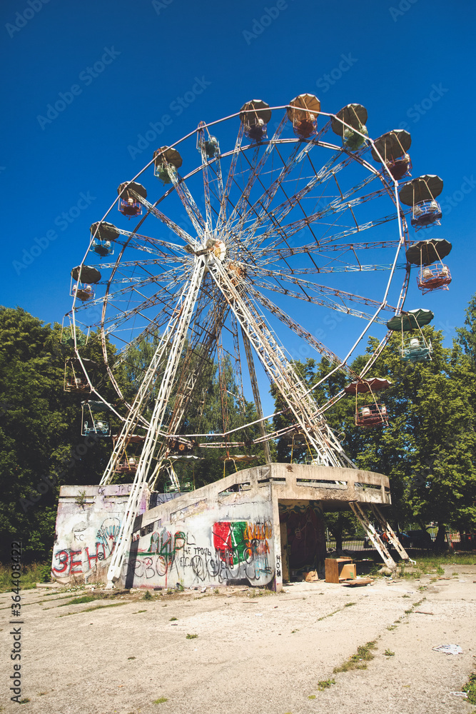 An old rusty ferris wheel in a closed abandoned USSR theme amusement park. Sad post apocalypse atmosphere in a sunny summer day.