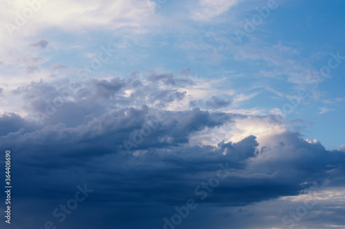 Dramatic rainy clouds on dark blue evening sky. Natural background with stormclouds and sunlights of setting sun.