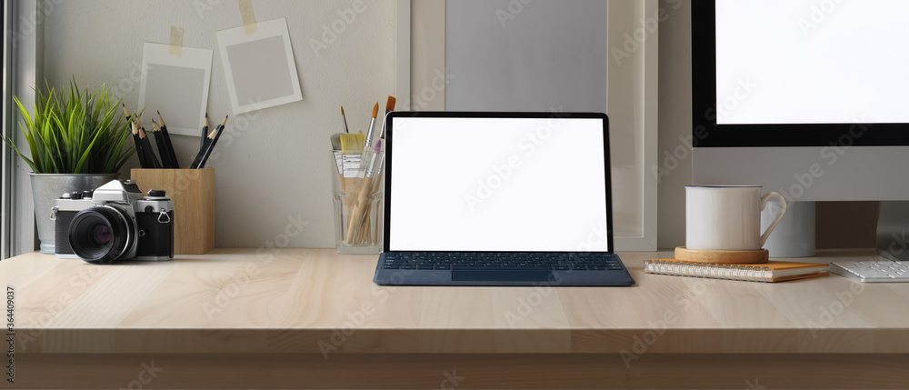 Simple worktable with mock up tablet, computer, camera, painting brushes, stationery and decorations in home office Simple worktable with mock up tablet, computer, camera, painting brushes, stationery and decorations in home office