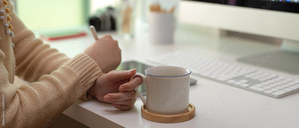 Female worker looking informations on tablet and holding coffee cup on white office desk in office room