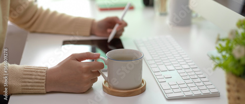 Female worker working on tablet and holding coffee cup on white office desk in office room