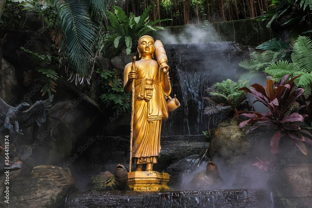 Golden Buddha statue in the tropical garden with waterfall in Wat Saket Golden Mountain Temple in Bangkok