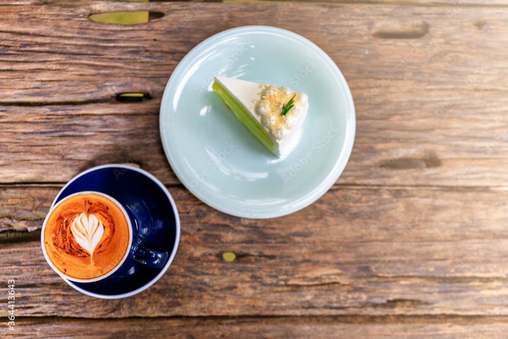 Top view of hot cappuccino coffee and home made cake in the cafe, Heart shaped cappuccino coffee in blue cup on a wooden table with copy space. Top view of hot cappuccino coffee and home made cake in the cafe, Heart shaped cappuccino coffee in blue cup on a wooden table with copy space.