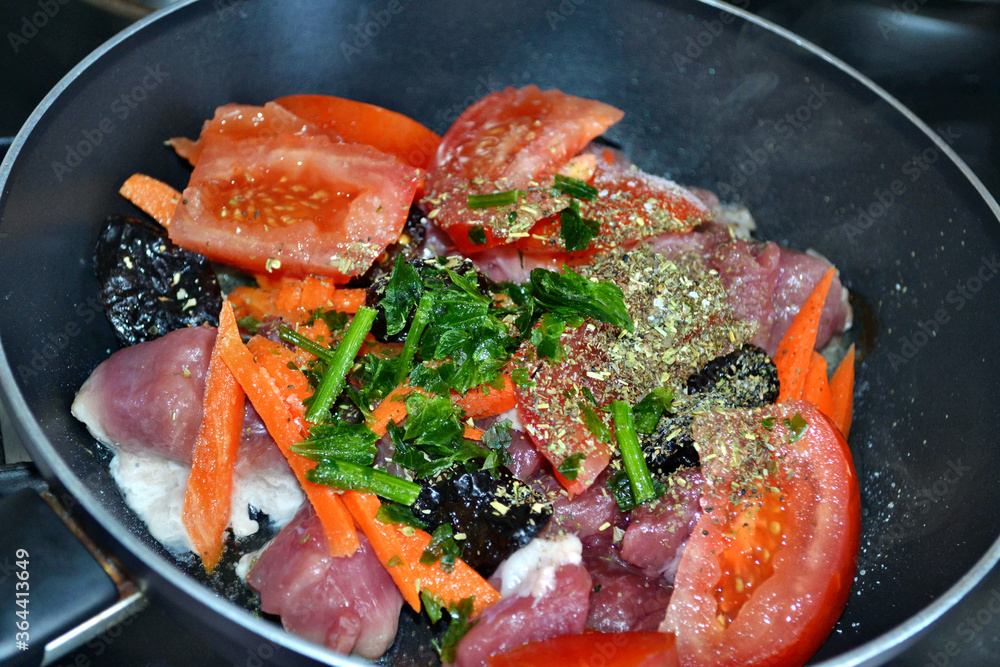 Initial braising of pork with vegetables, dried plums and spices in black braising pan. Closeup. Initial braising of pork with vegetables, dried plums and spices in black braising pan. Closeup.