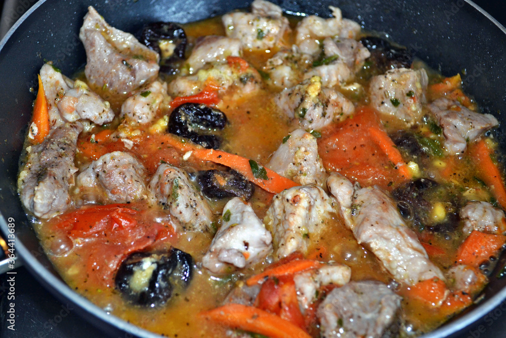 Braised pork with vegetables, dried plums and spices in black braising pan. Closeup. Braised pork with vegetables, dried plums and spices in black braising pan. Closeup.