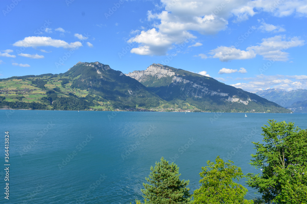Magnificent view of lake Thun and the Alps, Switzerland. Blue sky, blue water, boats, green trees. Sunny summer weather.