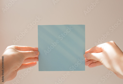  Blue square leaflet with hard shadows mock up on a white background in the hand of a young woman. School concept