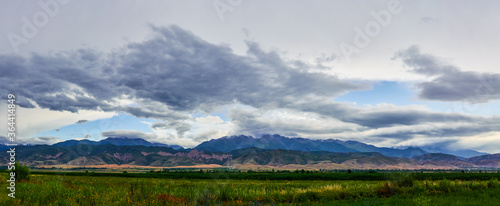 Panorama of a mountain valley in the summer, cloudy sky. Fairytale sunset over the mountain peaks, amazing nature, summer in the mountains. Travel. beautiful background picture of nature