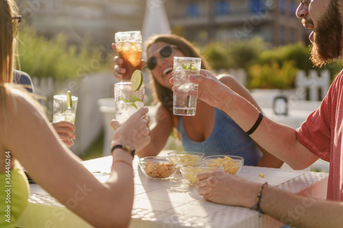 Happy hour toasting. Young friends clinking with fresh mojitos cocktails sitting in a counter restaurant and taking aperitif in the summer. Friendship and togetherness concept photo