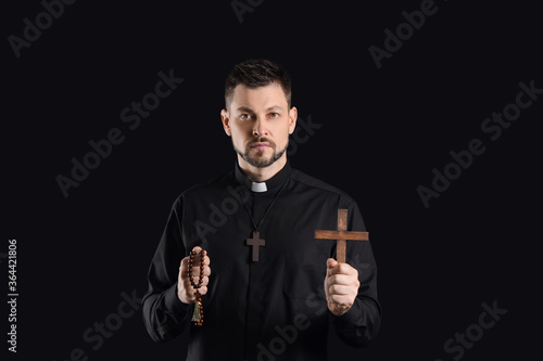Canvas Print Handsome priest with cross and rosary beads on dark background