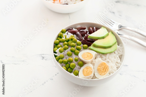 Bowl with tasty rice, beans, avocado and egg on table