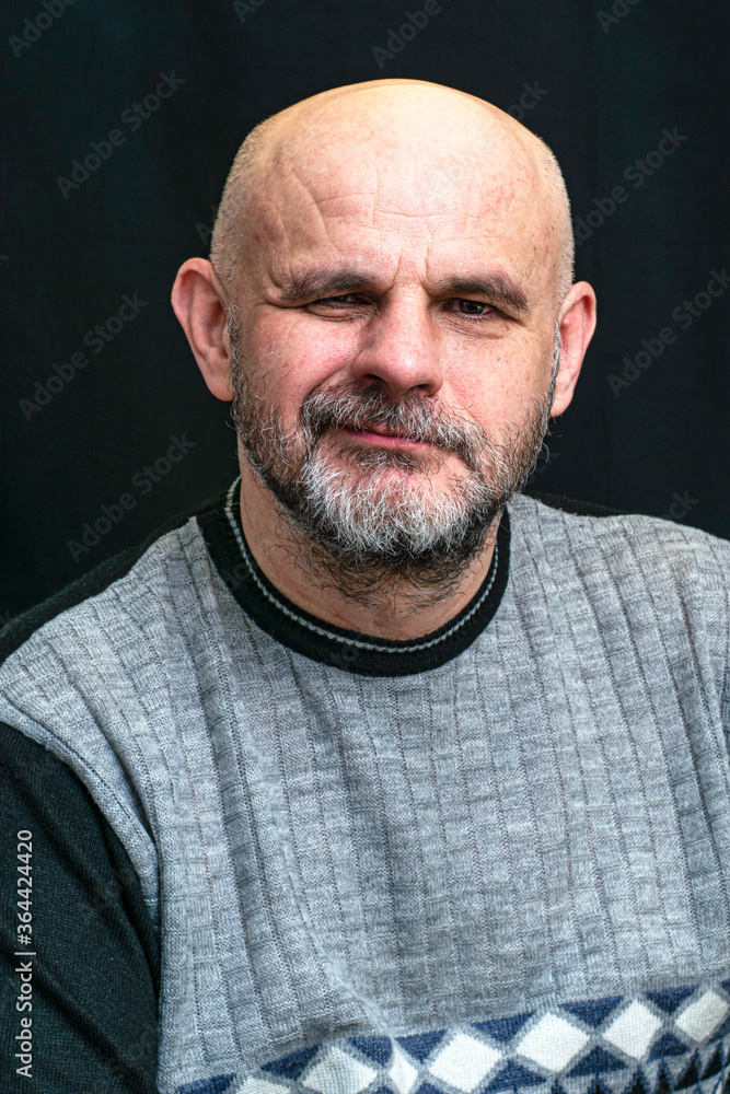 middle-aged bald bearded man grins contemptuously against the dark background middle-aged bald bearded man grins contemptuously against the dark background