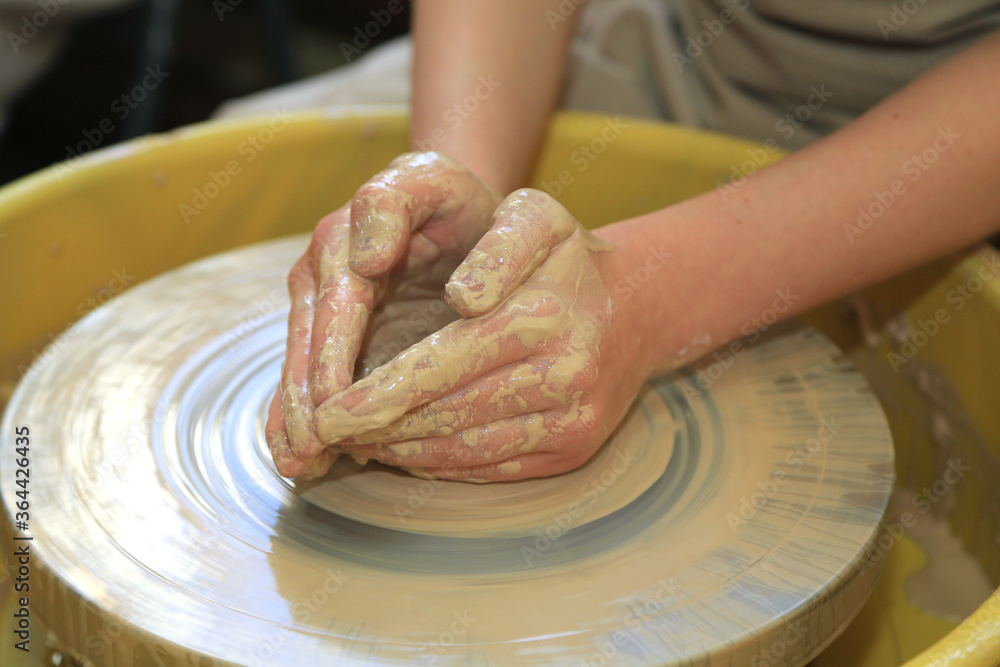 Creating a clay product on a pottery wheel in a pottery workshop. Hands sliding on clay. Art
