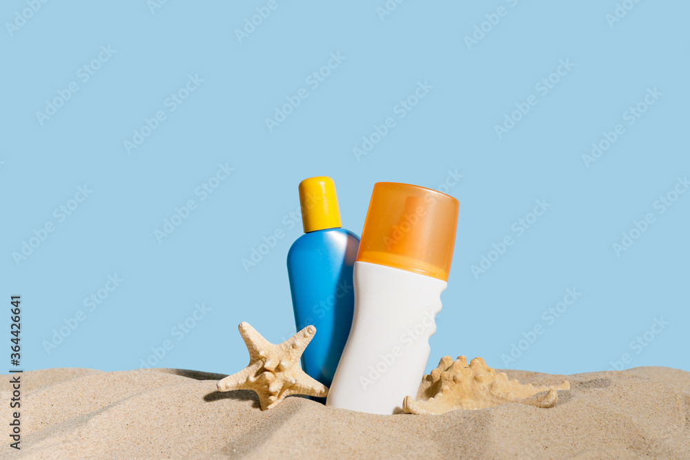 Bottles of sunscreen cream on sand against color background Bottles of sunscreen cream on sand against color background