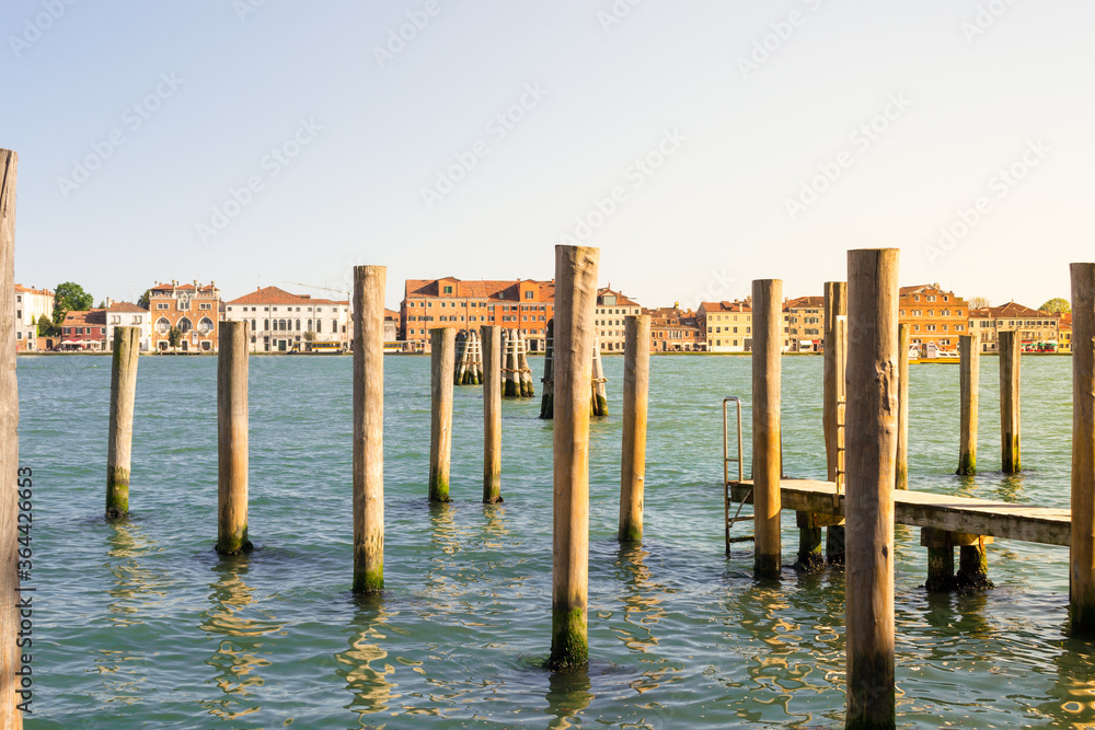 Venice, Italy. Typical landscape view of the lagoon, rawn of mooring poles in perspective with the peculiar venetian architecture in the background. Venice, Italy. Typical landscape view of the lagoon, rawn of mooring poles in perspective with the peculiar venetian architecture in the background.
