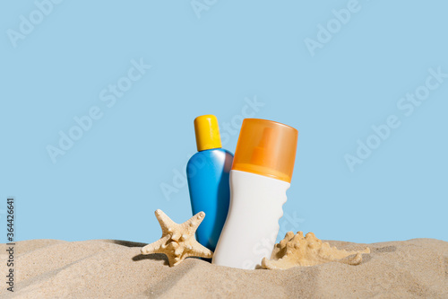 Bottles of sunscreen cream on sand against color background photo