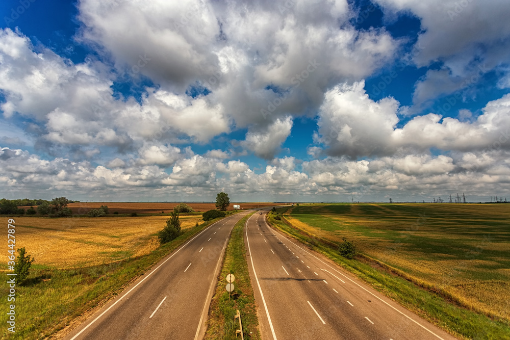 Highway from the height of the bridge, against the background of clouds, fields and blue sky