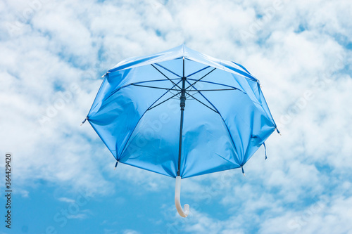 Blue umbrella floating in the bright blue sky and white cloud background.
