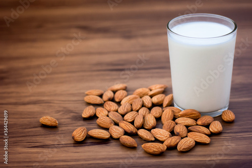 Closeup almond seeds and glass of almond milk isolated on wood table background. Natural protein and  Healthy drinks concept. Selective focus.