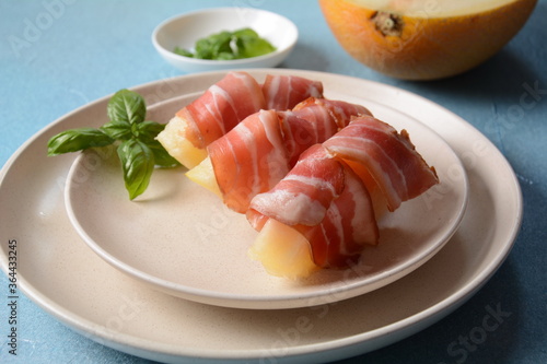 Summer appetizer with sweet melon and ham on blue background