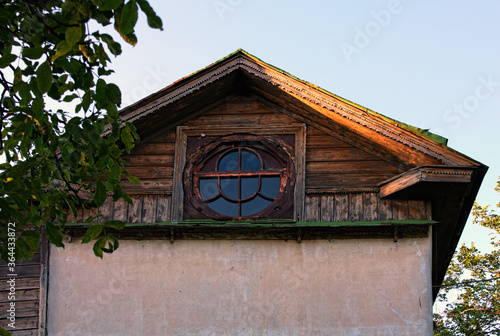 Ancient house with oval window in the attic against blue sky. Vintage house with roof decorated by the carved wooden platbands. Concept of historical buildings of ancient Ukraine