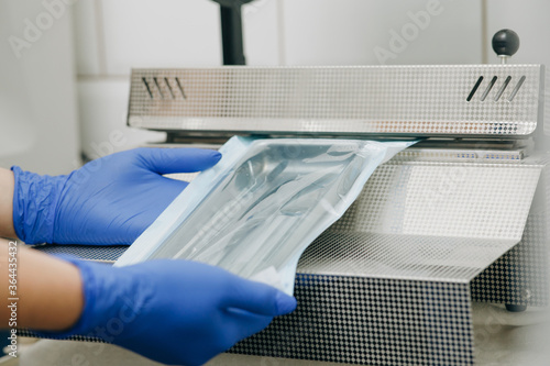 Foto Close up dentist's assistant hands in gloves packing dental instrument set for autoclaving in a plastic bag using vacuum packing machine