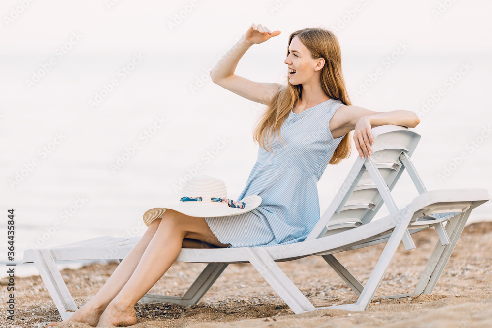 Relaxing beautiful girl in a summer dress, relaxing on a sandy beach, lying on a chaise longue. Summer vacation, travel, sea