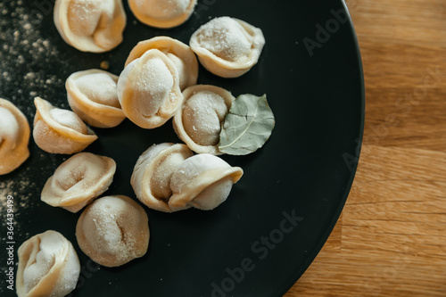 Stuffed homemade dumplings on a dark plate on wooden table. Russian pelmeni.