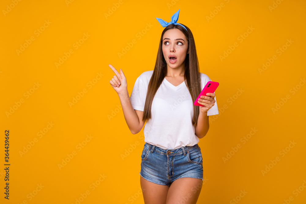Look unbelievable ads. Astonished girl use smartphone point finger copyspace demonstrate social media promotion wear blue headband t-shirt denim jeans shorts isolated bright color background Look unbelievable ads. Astonished girl use smartphone point finger copyspace demonstrate social media promotion wear blue headband t-shirt denim jeans shorts isolated bright color background