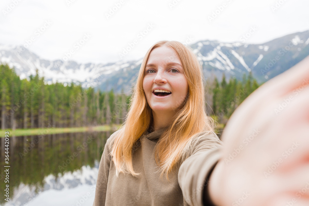 The girl tourist taking selfie in the mountain lake. Looking at camera and smile. Travel and active life concept. Outdoors