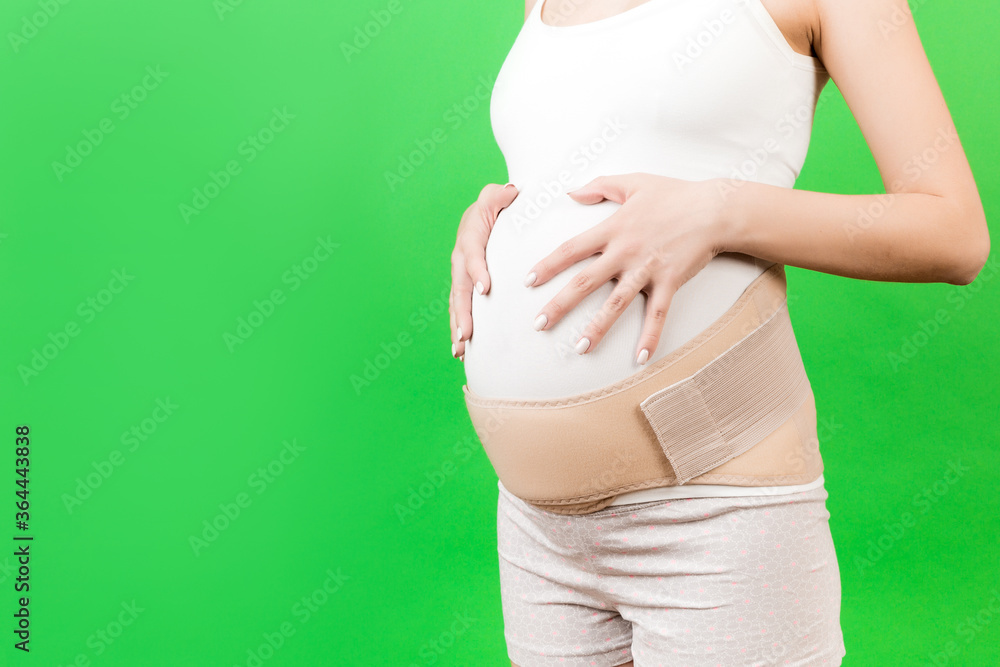 Cropped image of supporting bandage on pregnant woman at green background with copy space. Orthopedic abdominal support belt concept Cropped image of supporting bandage on pregnant woman at green background with copy space. Orthopedic abdominal support belt concept