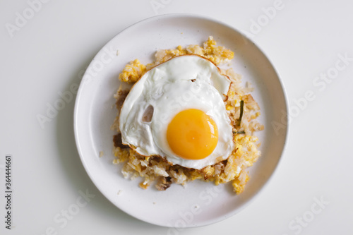 Homemade fried rice with fried egg on top served on white dish.