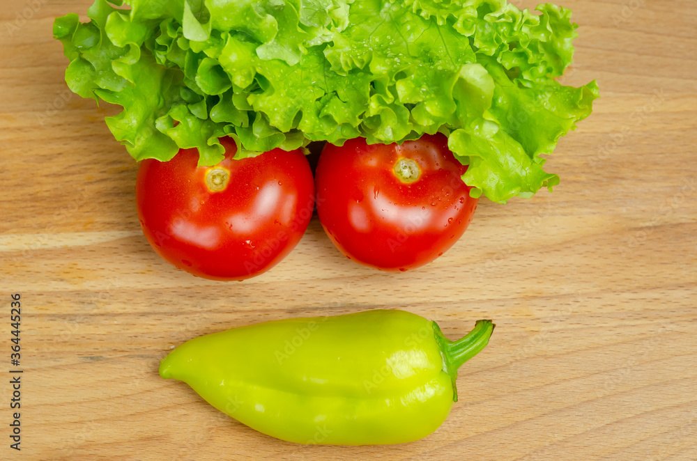 Fresh juicy vegetables peppers, tomatoes, cucumbers lettuce leaves with water drops are beautifully laid out on a wooden Board close-up. Vegetables are in the form of a funny face, top view Fresh juicy vegetables peppers, tomatoes, cucumbers lettuce leaves with water drops are beautifully laid out on a wooden Board close-up. Vegetables are in the form of a funny face, top view